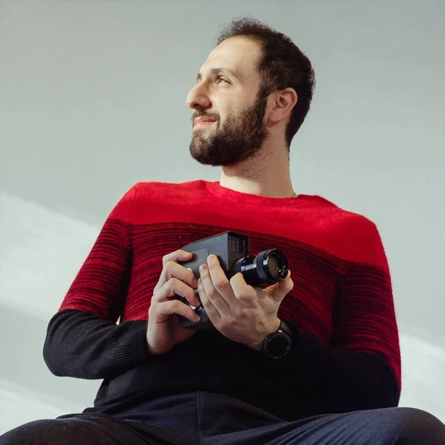 a man sits in front of a grey backdrop holding an electronic camera