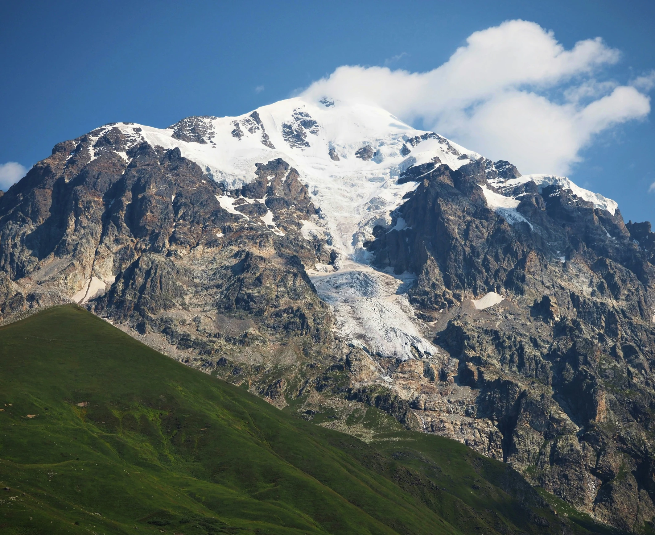 a white and grey snowy mountain side with green grass