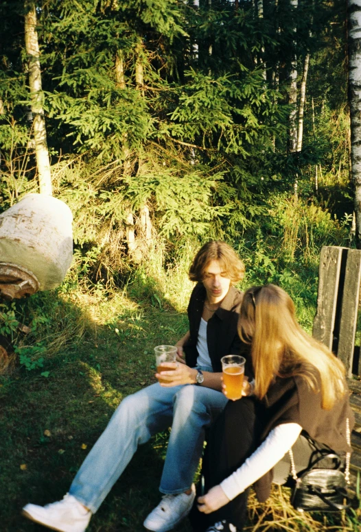 two people sitting outside on the ground holding drinks