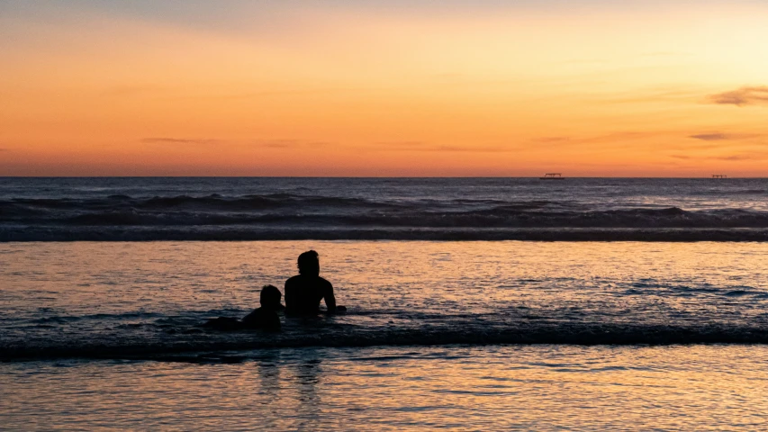 the silhouette of a person sitting in the water as sun sets