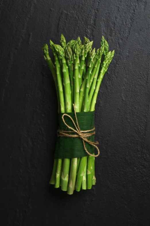 some asparagus tied up with a green string on a black surface