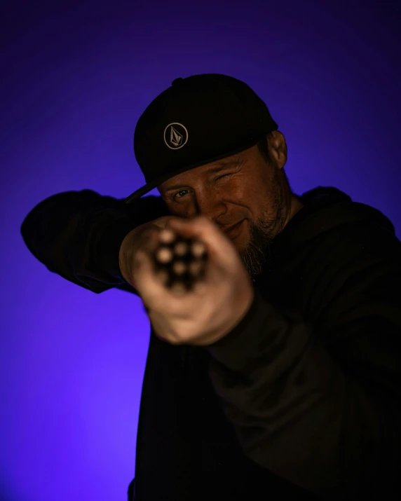 a man with a baseball cap on, pointing to the camera