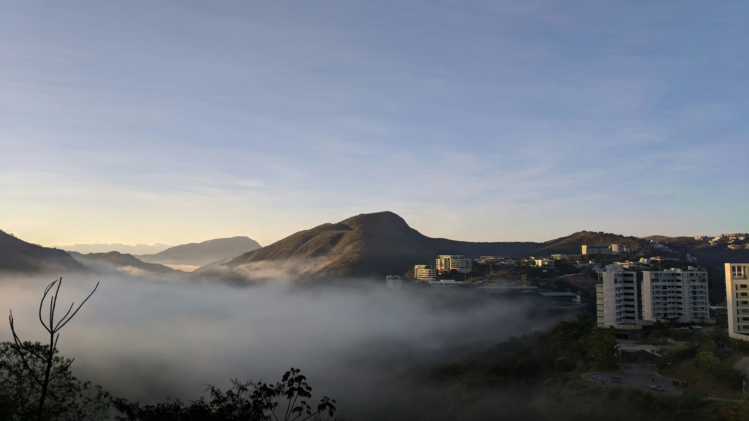 mountains and buildings covered in fog with city visible behind them