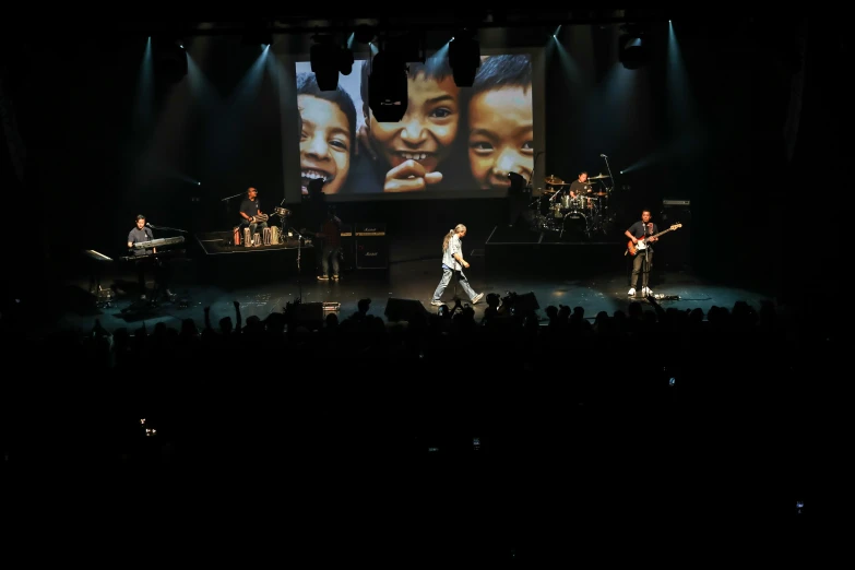 two large screens on a darkened stage with people watching