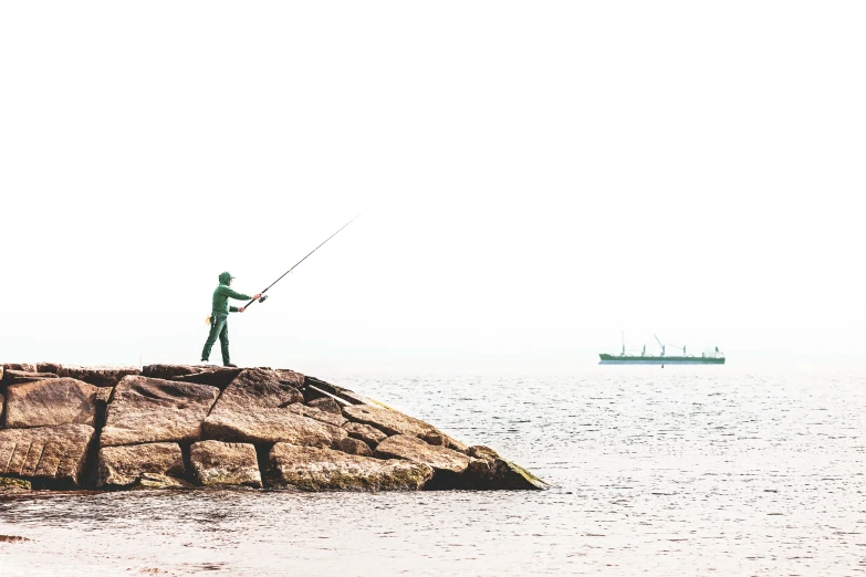 two people fishing off rocks off the coast of a large body of water