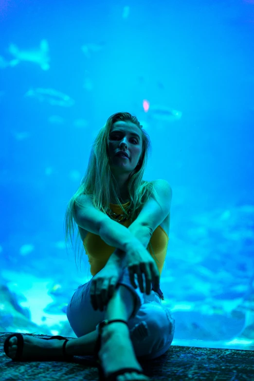 a young woman sits in front of a giant aquarium tank