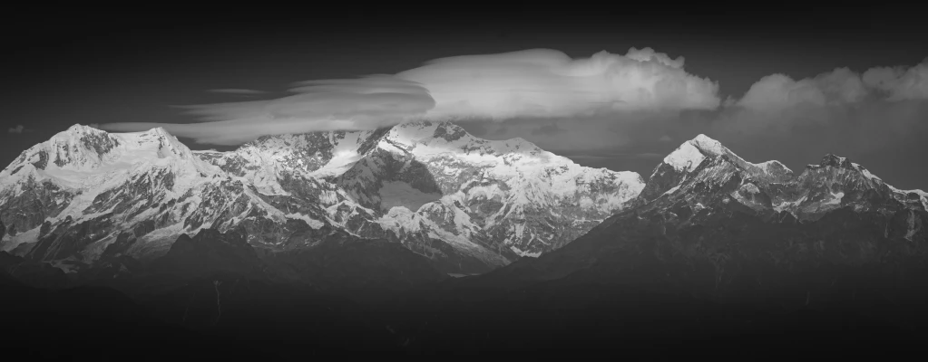 a cloudy mountain top over some snow capped mountains