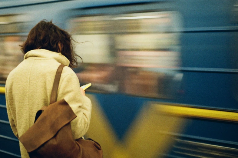 a woman standing in front of a train with a brown bag