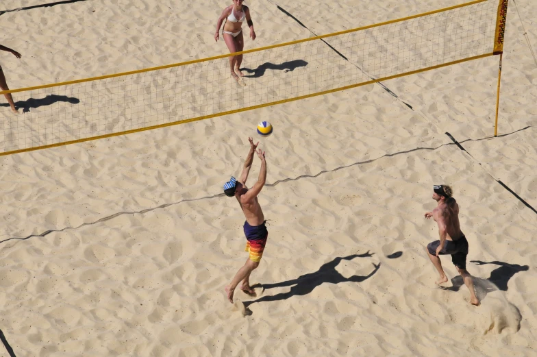 people playing volleyball on a sandy beach with sand and grass