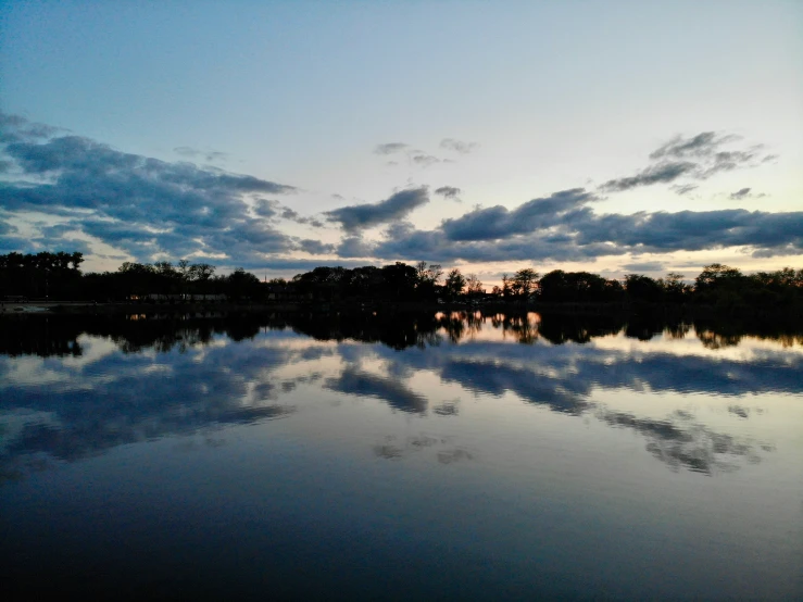 a lake at sunset with some clouds reflected on it