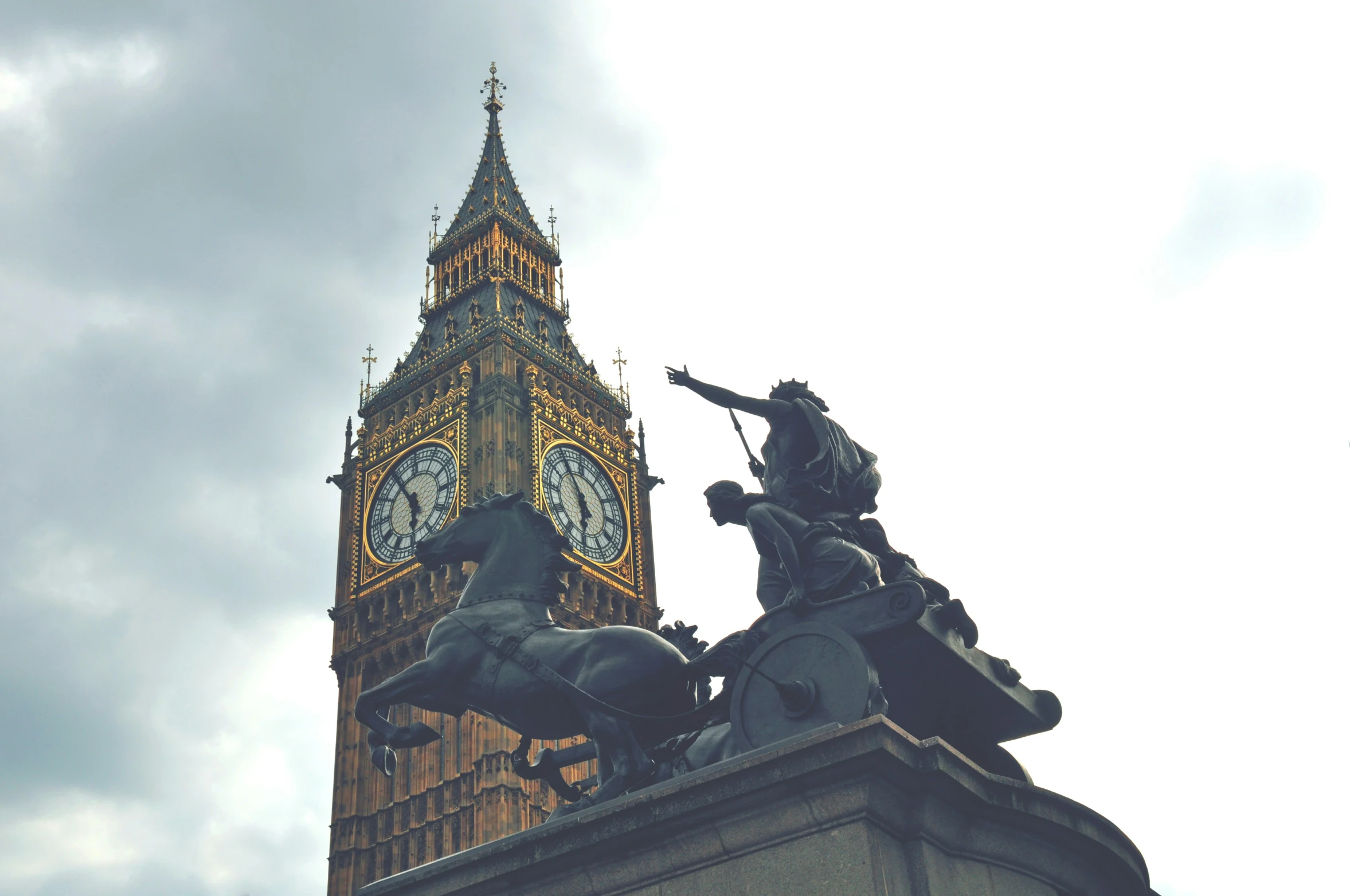 a clock tower sitting behind a statue of two men on horses