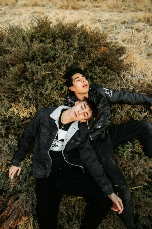 two young men laying in the grass in front of shrubbery