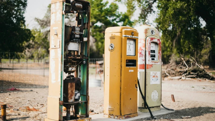 two yellow gas pumps in the middle of a dirt area