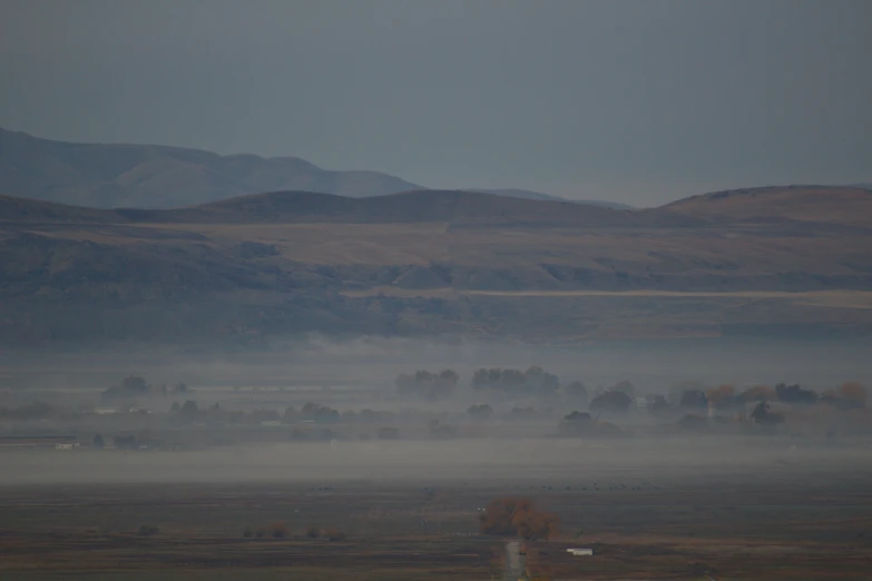 fog covers farmland, mountain range in the background