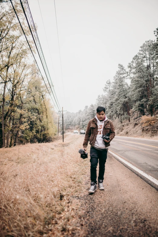 a young man walking down the road with a backpack and hat on