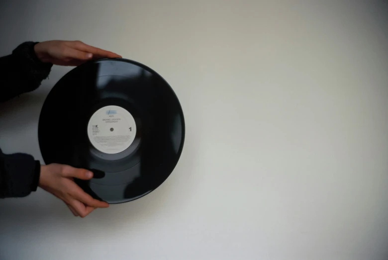 a hand holding a black record next to a white wall