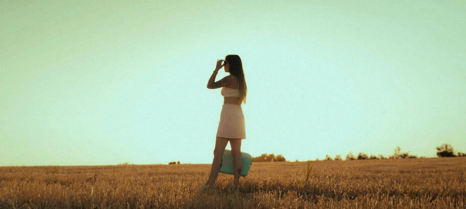 a woman stands in a wheat field on a cell phone