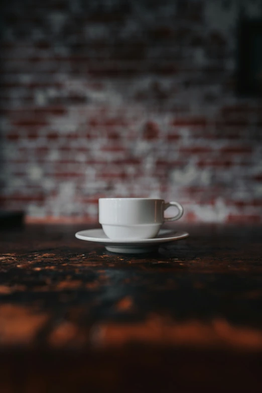 an empty coffee cup on a table against a brick wall