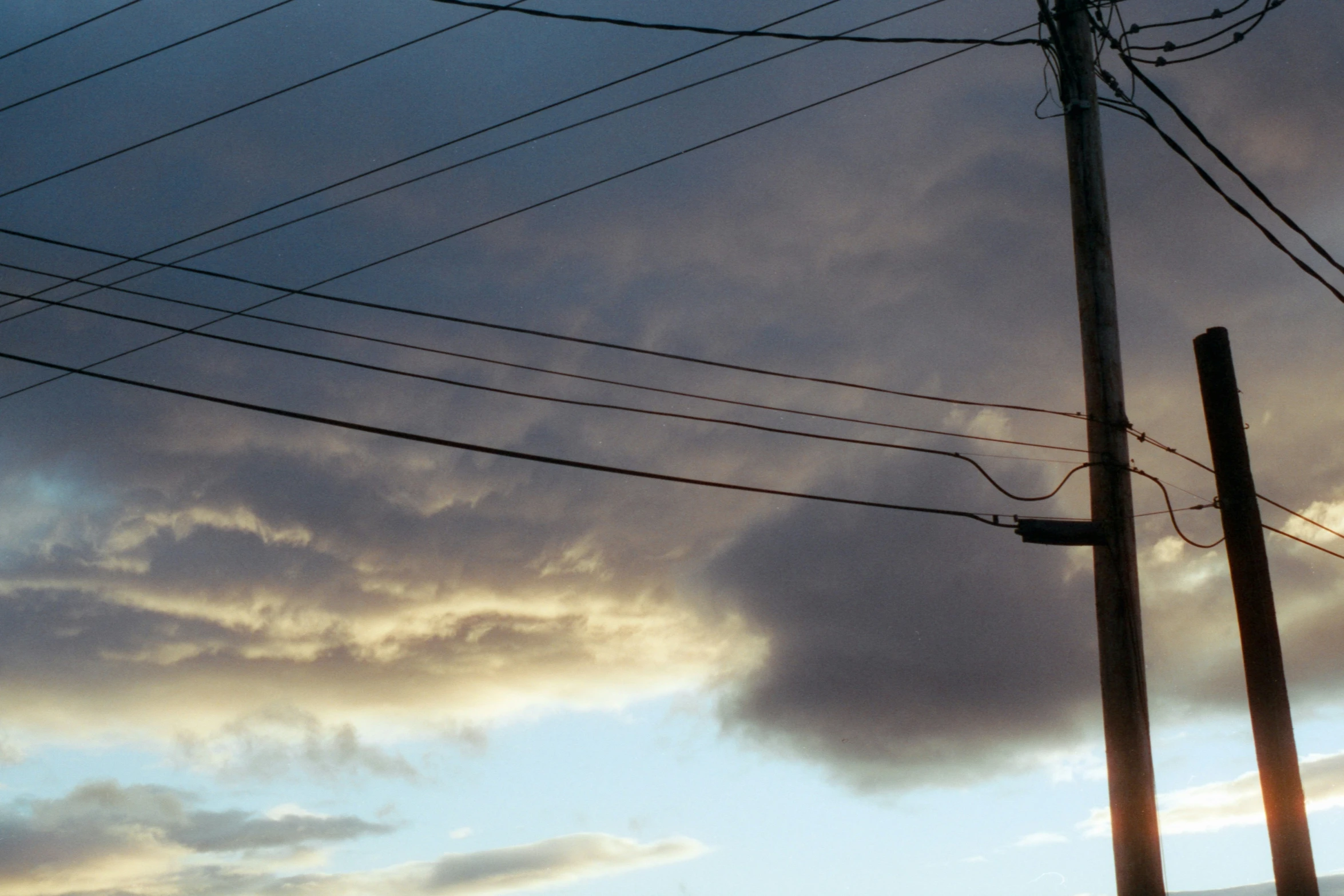 a cloudy sky with the sun setting behind wires