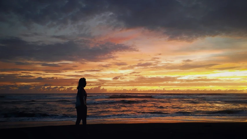 a man stands alone on the beach at sunset