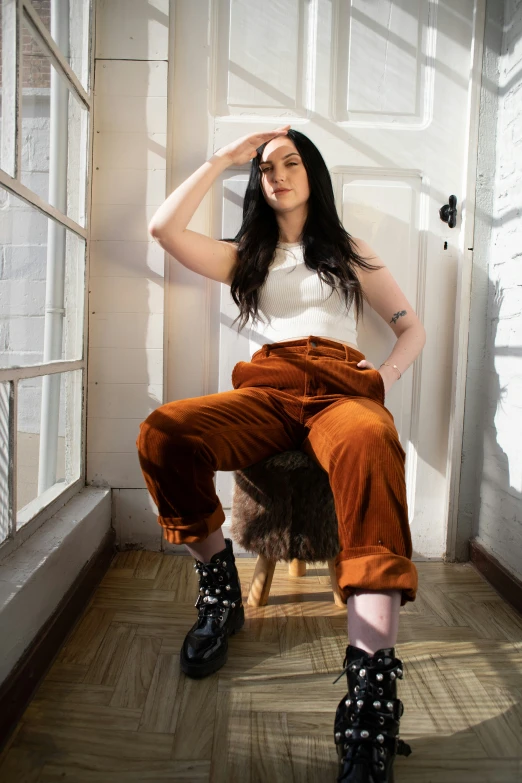a woman in an orange velvet pants sits by a window
