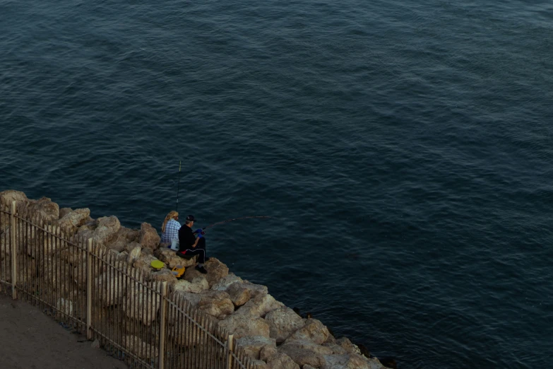 two people sitting by the ocean watching fishing