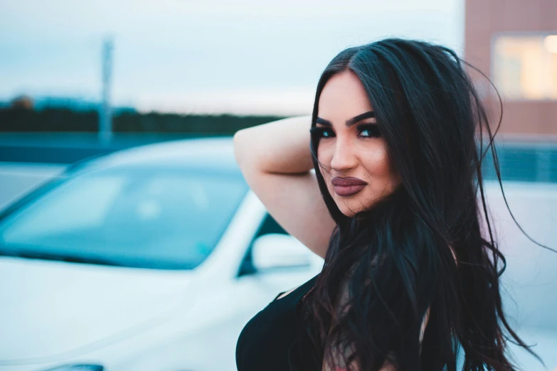 a woman with long hair stands near a white car