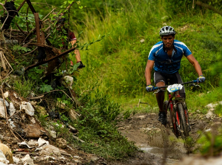 a man in blue shirt riding on muddy path next to bushes