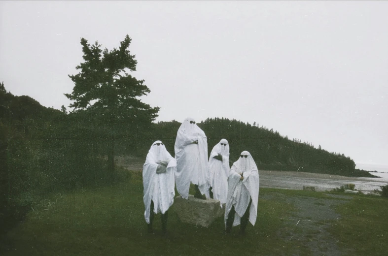 three ghostly figures in white robes walking towards the ocean