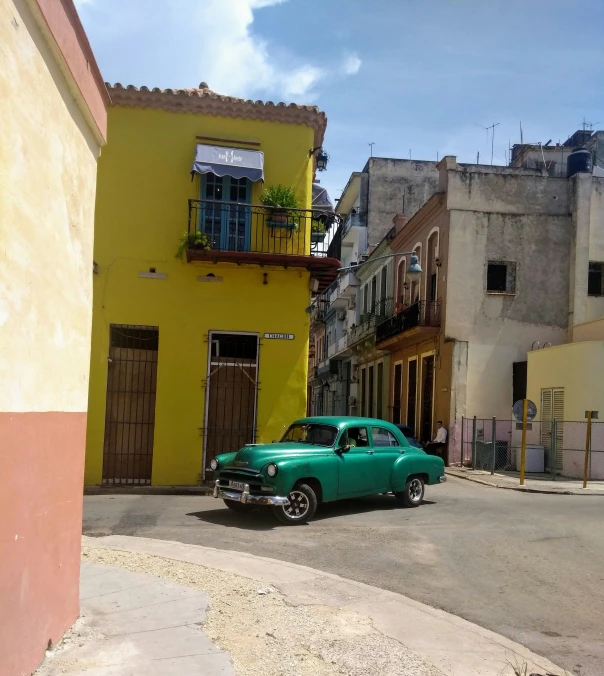 a old green car parked next to a yellow building