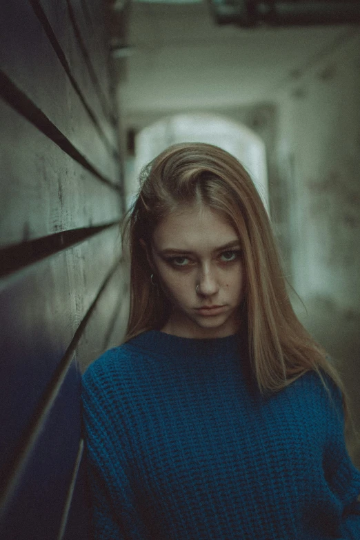 a beautiful blond in a blue sweater next to a wall