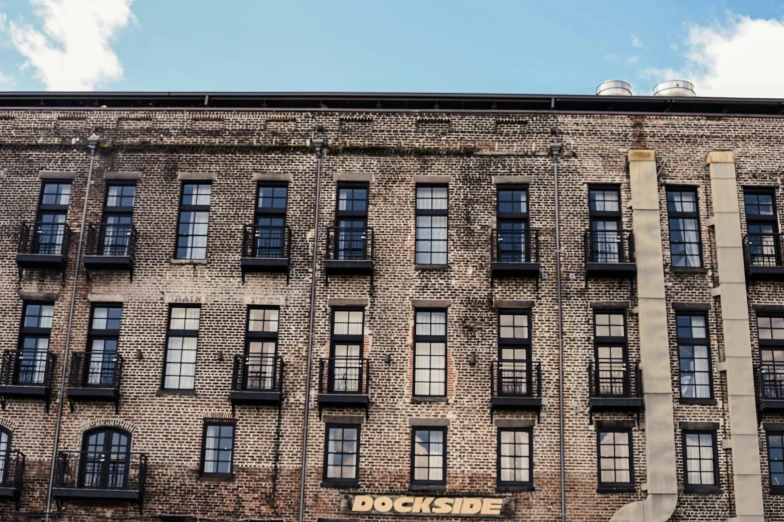 a brick building with lots of windows next to a white cloud filled sky