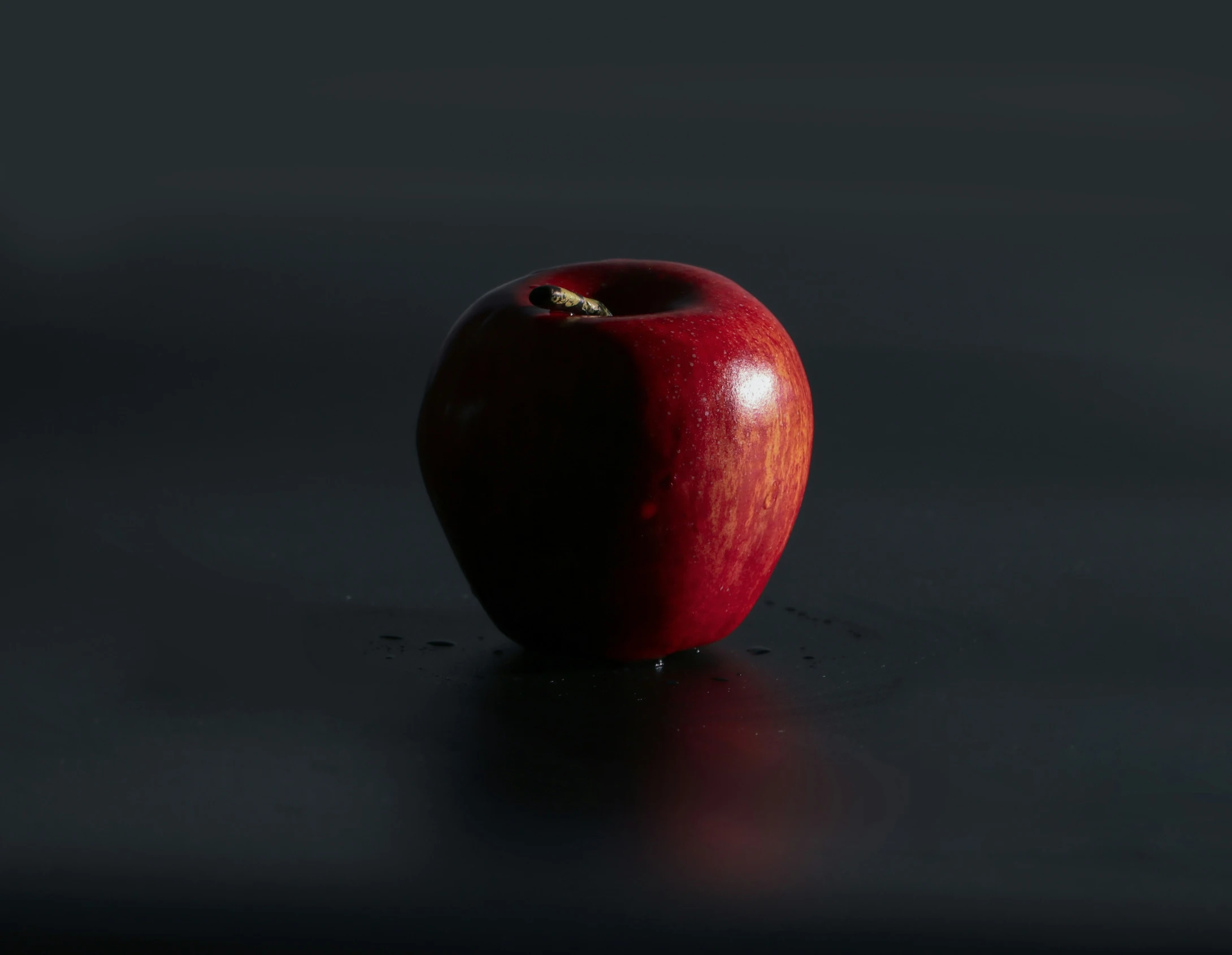 an apple sitting on top of a table on a dark surface