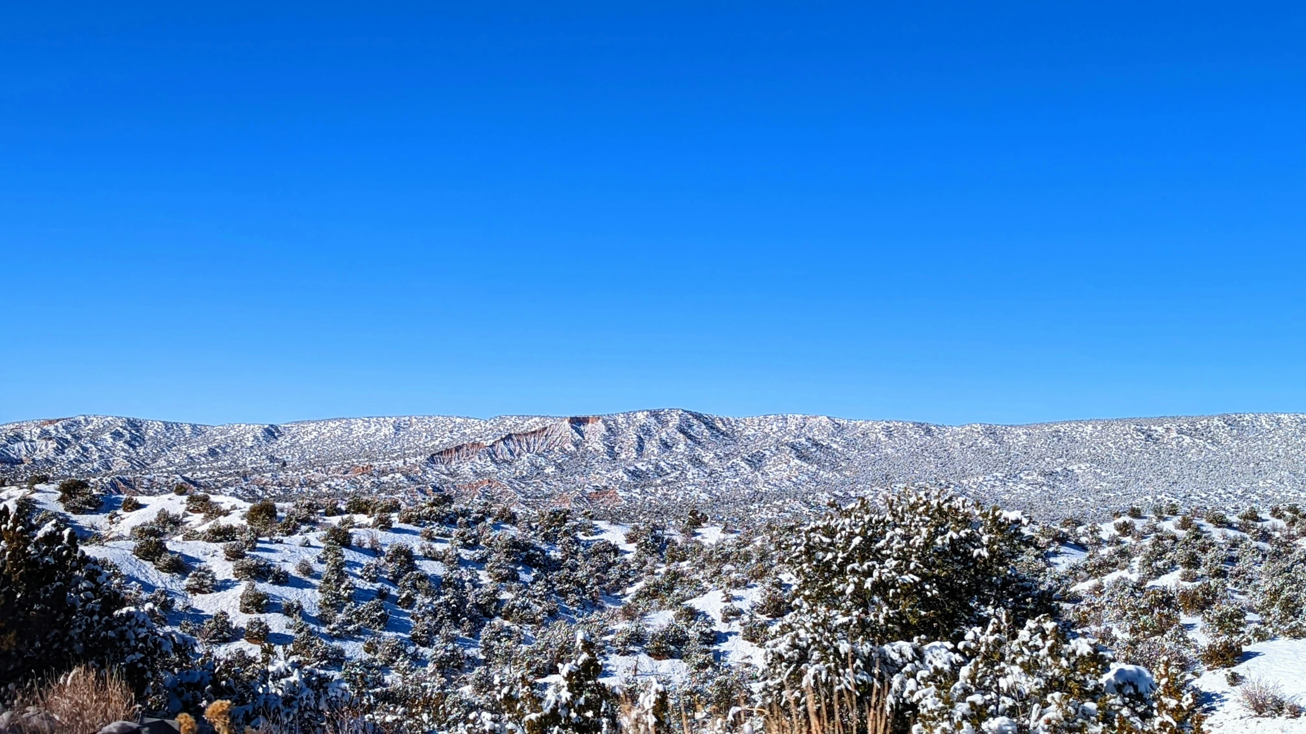 a blue sky with clouds and small hills covered in snow