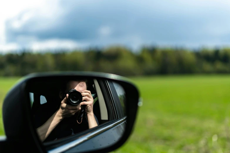 a man holding a camera up to the side of his car's mirror