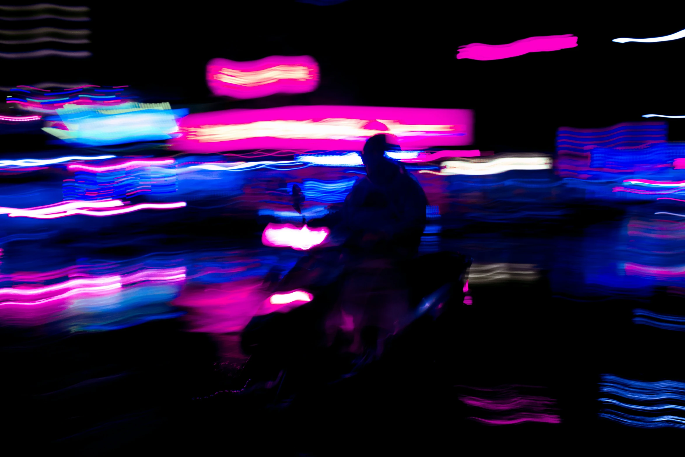 a silhouette of a man on a motorcycle with blurry lights