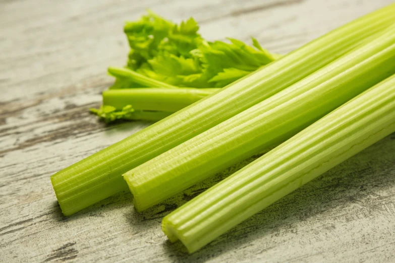 three celery stalks on a wooden surface next to some small leaves