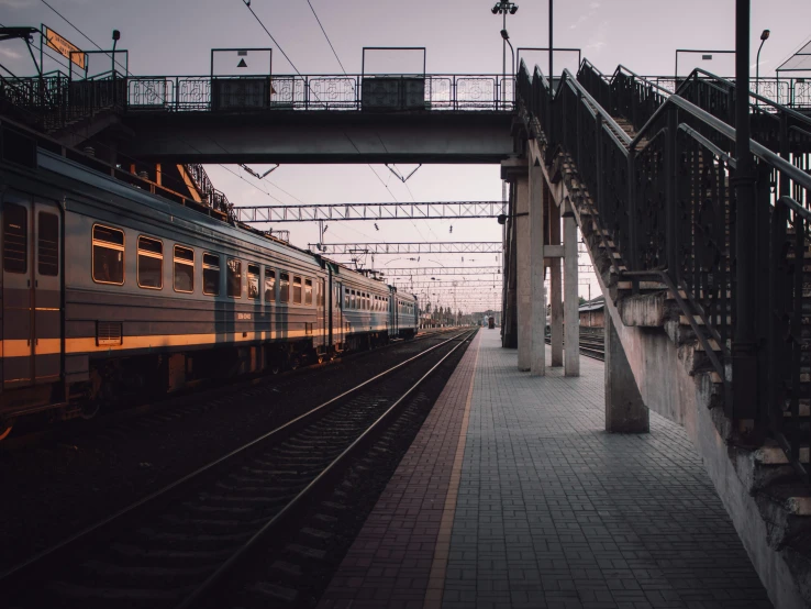 the sun is setting on a railway station with a large train coming out of the tunnel