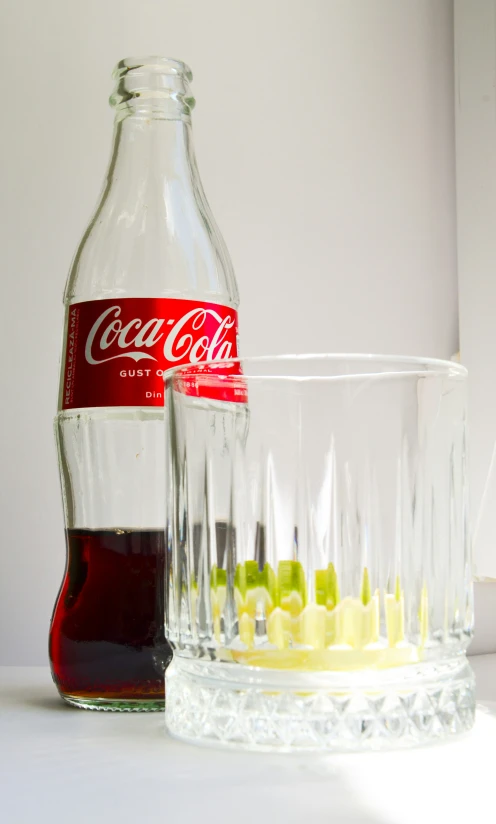 a coke bottle is sitting next to a glass filled with colored fruit juice