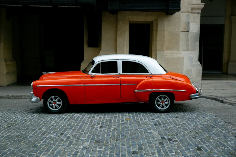 an old orange car parked on a brick street