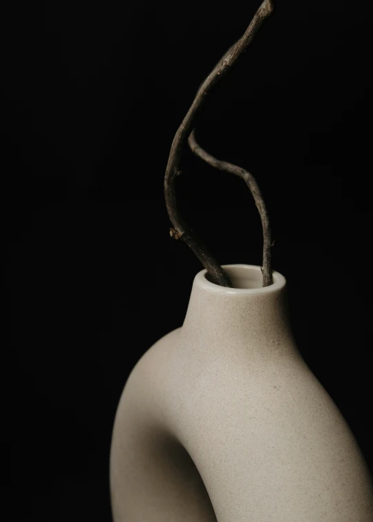 a white vase with a twig sticking out of it