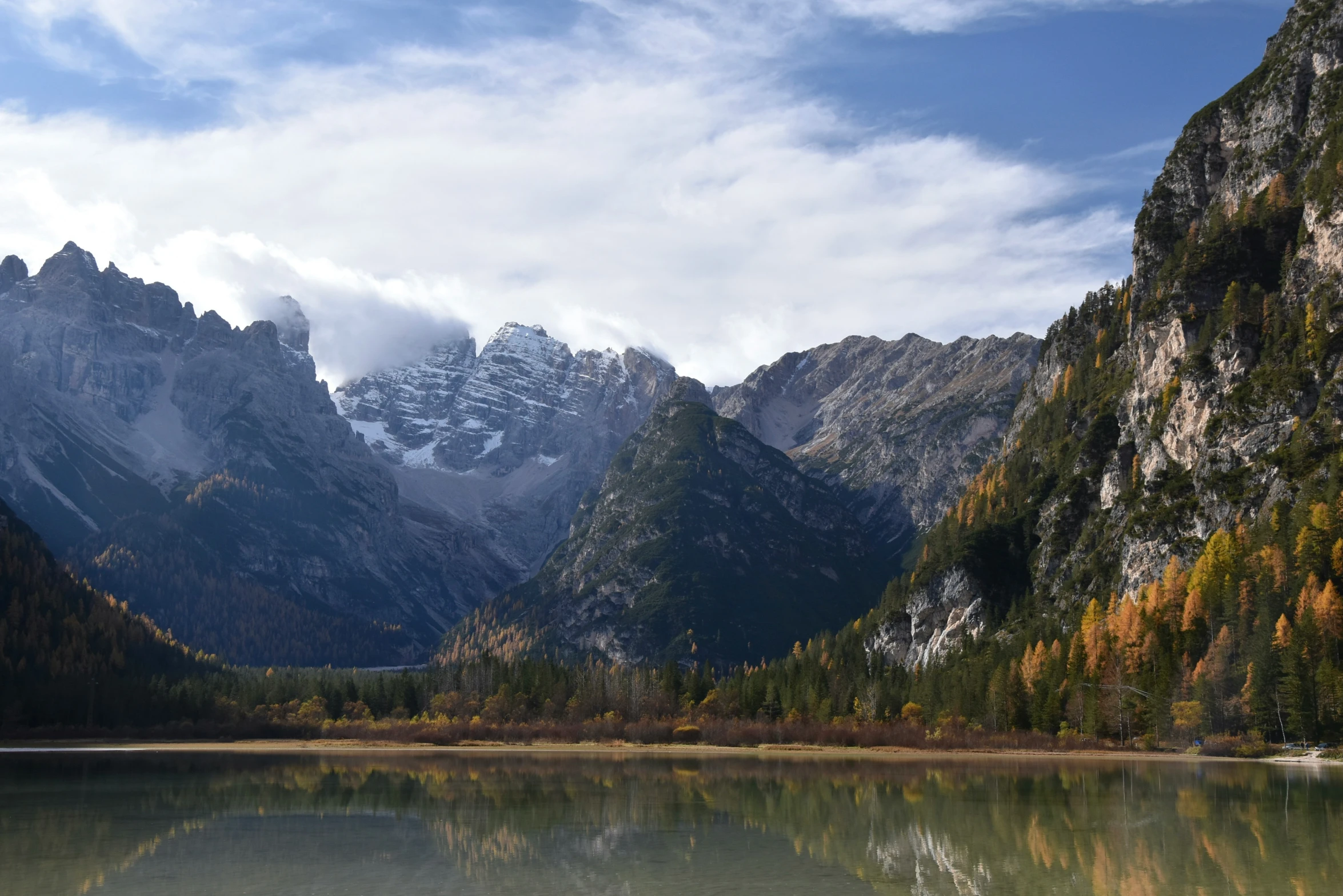 a mountain range is covered with snow and a lake surrounded by evergreen trees