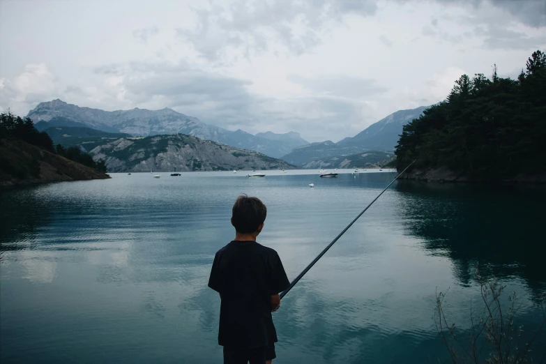 a boy is holding a rod and standing on the shore