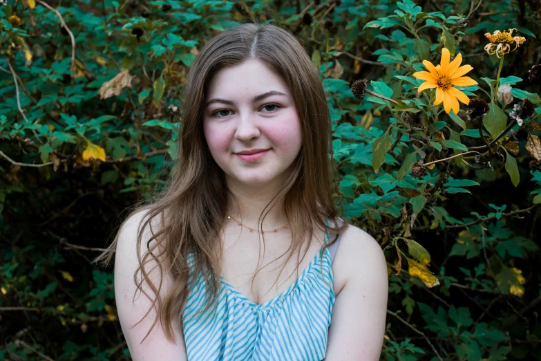 a young woman posing by a bush with sunflowers in the background