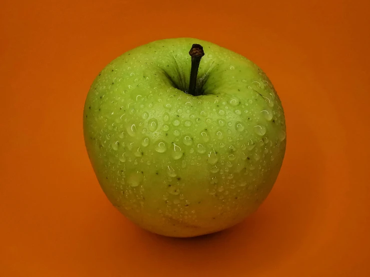 an green apple is on orange with drops of water on the surface