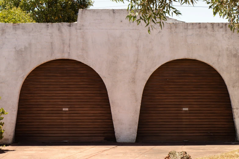 two large arched doors on a wall next to a sidewalk