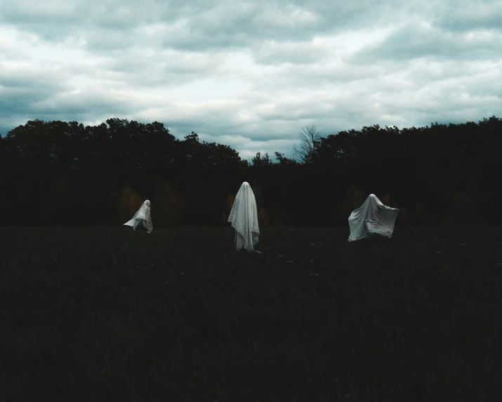 three ghostly women in a field on a cloudy day