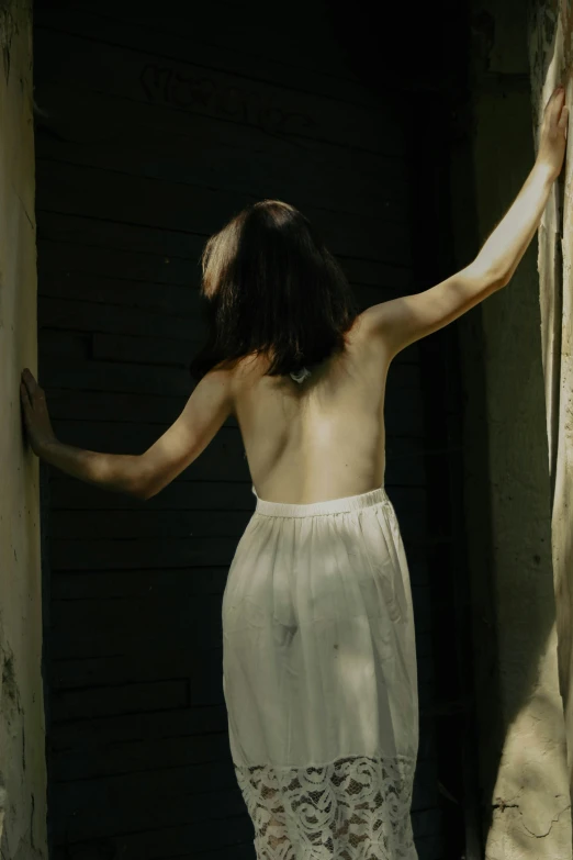 a woman in white clothing standing by a brick wall