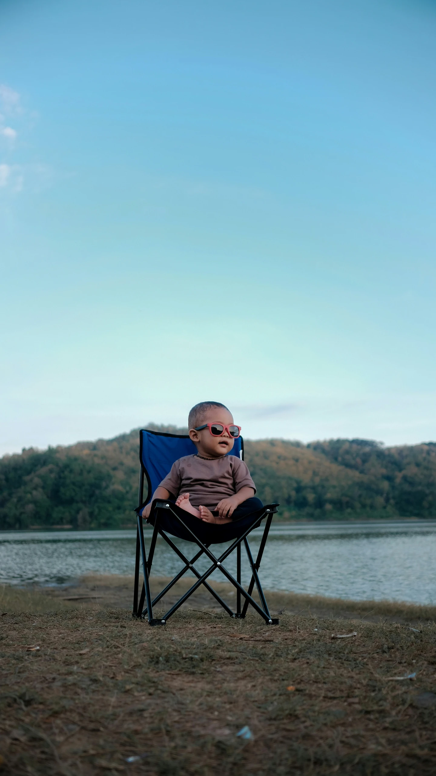 baby sitting on a folding chair by the water