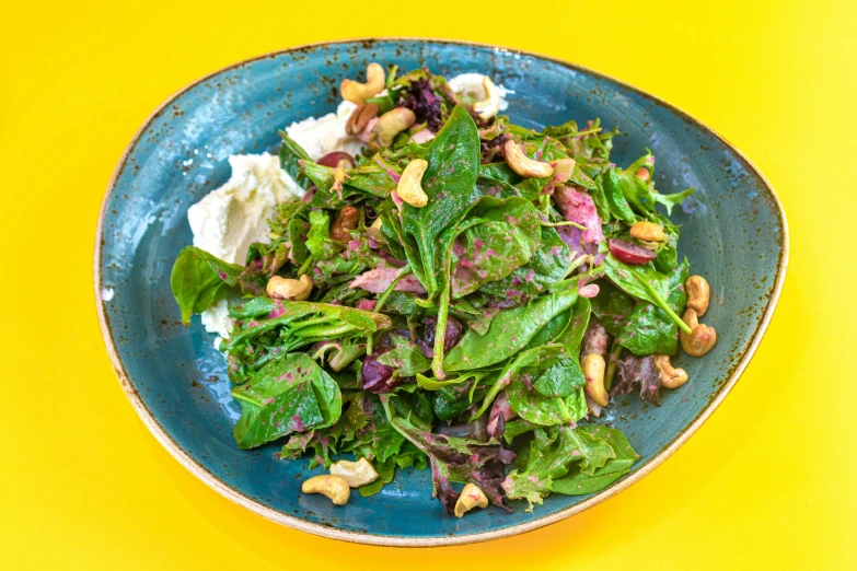 a blue bowl with a green salad on top of a yellow table